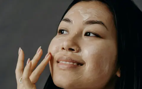 Donna applica una crema sul viso, un gesto quotidiano per come curare la pelle del viso.