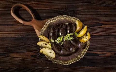 Kaszanka z piekarnika podana z pieczonymi ziemniakami i szczypiorkiem na ozdobnym talerzu.