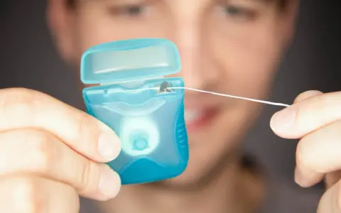 Mężczyzna trzyma niebieskie pudełko z nicią dentystyczną (floss).