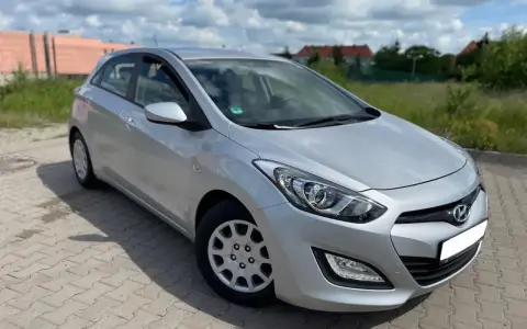 Srebrny Hyundai i30 1.4 benzyna zaparkowany na kostce brukowej, w tle zielona trawa i budynki.