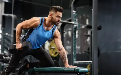 Mann mit Bart macht einbeiniges Rudern mit Kurzhantel. Fokus auf Muskelaufbau Training im Fitnessstudio.