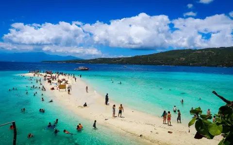 Plaża na Filipinach z turystami kąpiącymi się w turkusowej wodzie i spacerującymi po piaszczystym brzegu.