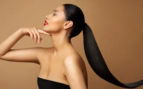 Frau mit glänzendem, schwarzem Pferdeschwanz und rotem Lippenstift, die ihren Hals berührt. Ihr **sleek look** unterstreicht ihre Eleganz.