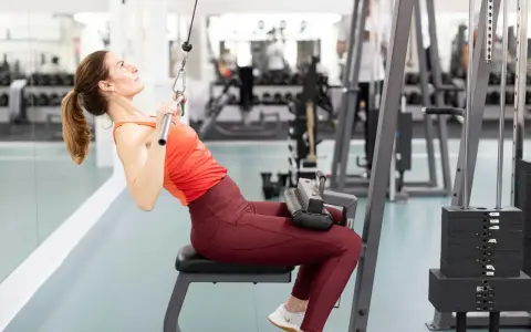 Kvinna tränar rakarmade latsdrag på gym.