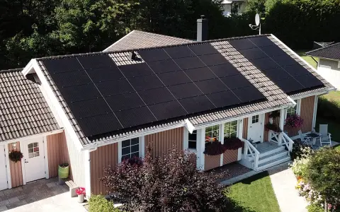 Ett hus med mörka solceller på taket, som fångar solens energi för ett grönare hem.