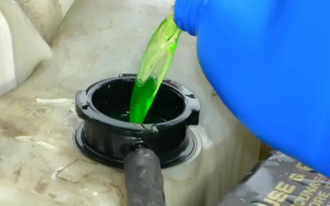 Green antifreeze is poured from a blue jug into a car's coolant reservoir. This raises the question: does antifreeze expire?