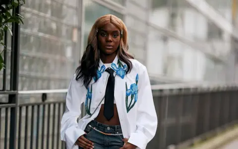 Modella con jeans baggy, un capo che simboleggia libertà e stile informale, indossa una camicia bianca con ricami floreali e cravatta.