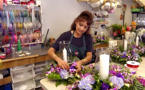 Florystka tworzy nowoczesne kompozycje kwiatowe z liliami i hortensjami. W tle widać półki z wstążkami, jak sprawdzić portfolio florysty pod kątem nowoczesnych kompozycji.