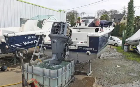 Un homme effectue le rinçage moteur hors bord vinaigre blanc d'un bateau. L'hélice est immergée dans une cuve remplie de liquide.
