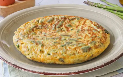 Tortilla de esparragos dorada y esponjosa, con trozos verdes de espárragos integrados en el huevo.