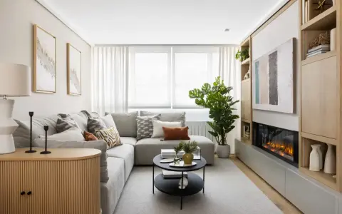 Acogedora decoracion salon pequeño con sofá gris, chimenea moderna y estanterías de madera.