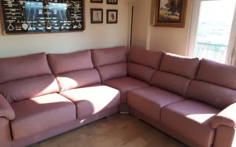 Cómodo sofá rinconera rosa, ideal para decorar salón. En la pared, un cuadro de nudos marineros y pinturas.