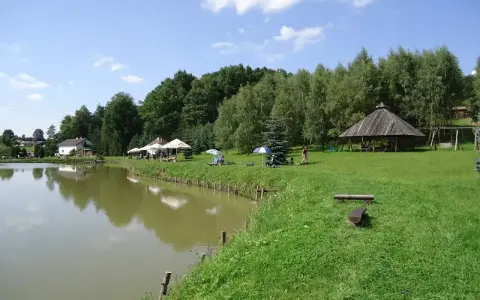 Malownicze dzikie łowiska Małopolska: spokojna woda, zielone wzgórza, drewniana altana i miejsca do wypoczynku.