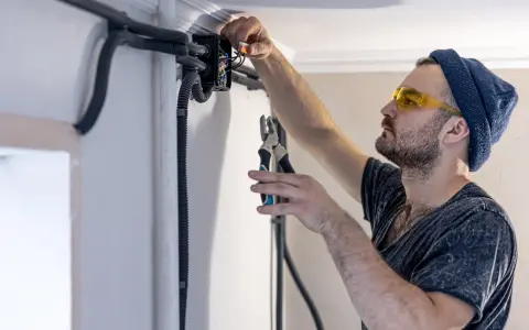 Elektryk w okularach ochronnych montuje przewody bezhalogenowe w puszce instalacyjnej, używając szczypiec.