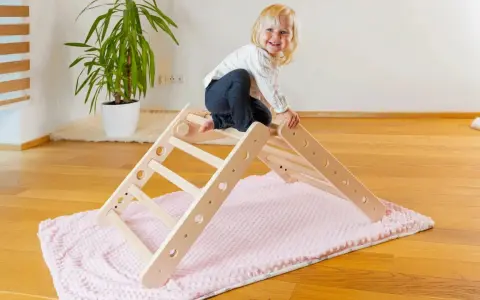 Ein fröhliches Kleinkind erkundet ein Pikler Dreieck. Ab wann Kinder damit spielen können, hängt von ihrer Entwicklung ab.