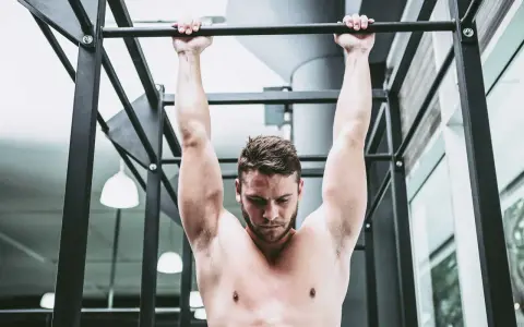 Uomo a torso nudo esegue trazioni alla sbarra, concentrato sul movimento per rafforzare la muscolatura.