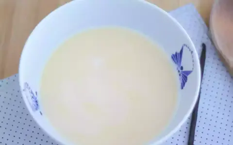 En skål med krämig vaniljsås, perfekt för ditt vaniljsås recept. En vaniljstång ligger bredvid.