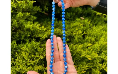Collana di cianite blu, con perle luminose che catturano la luce, tenuta tra le mani su uno sfondo verde.