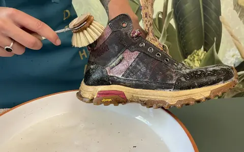 Schuhbürste reinigt schmutzige Wanderschuhe in Seifenwasser. So pflegen Sie Ihre Wanderschuhe richtig.