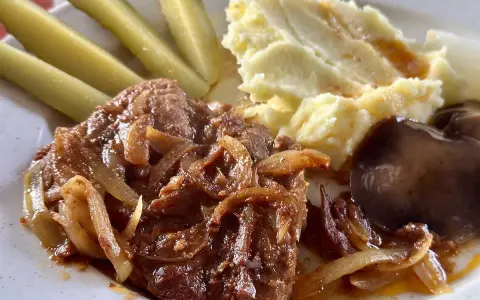 Karkówka pieczona w plastrach z cebulą, podana z puree ziemniaczanym, ogórkami kiszonymi i grzybami.