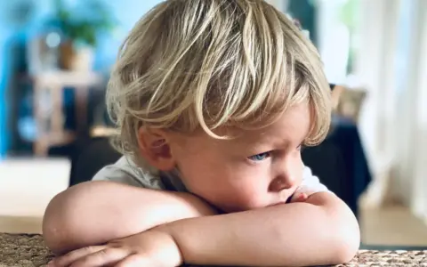 Ein blondes, sensibles Kind mit blauen Augen liegt auf den Armen und schaut nachdenklich zur Seite.