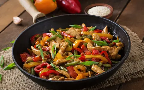 Straccetti di pollo con peperoni colorati e fagiolini, un piatto saporito e invitante servito in padella.