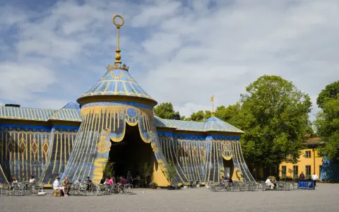 Blå och guldfärgad cirkustältliknande byggnad med uteservering i Haga parken.