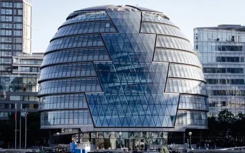 Edificio iconico di Norman Foster, con facciata a diamante in vetro, riflette il cielo e gli edifici circostanti.