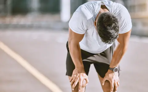 Atleta esausto con la testa china, mani sulle ginocchia, forse uno dei sintomi di overtraining.