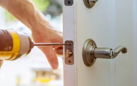 Main tenant répare une serrure cassée sur une porte fermée. Un tournevis est utilisé pour fixer le mécanisme.