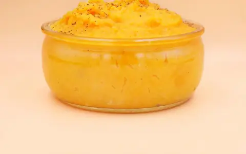 Pomarańczowe puree z batatów w szklanym naczyniu, posypane pieprzem.