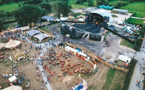 Vista aérea de un festival al aire libre con un gran escenario, carpas, puestos de comida y mucha gente disfrutando del summerfest Cerdanya.