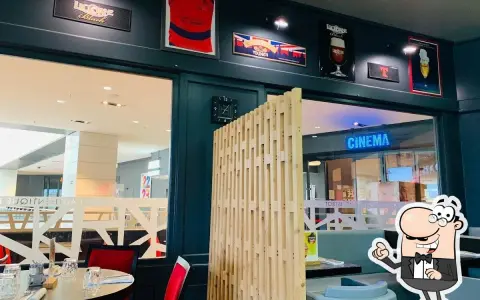 Ambiance chaleureuse à la trattoria Ibos, avec des décorations de rugby et de bière. Une enseigne "CINEMA" brille au loin.