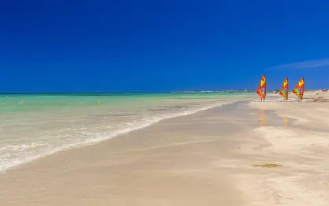 Piękna pogoda w Tunezji w marcu. Trzy kolorowe deski windsurfingowe na piaszczystej plaży, turkusowa woda i błękitne niebo.