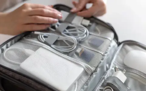 W torbie podróżnej schludnie ułożone kable, ładowarki i powerbank do samolotu. Dłonie porządkują zawartość.
