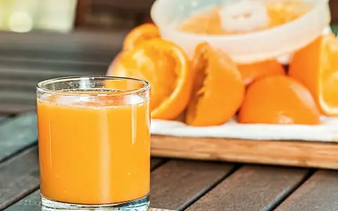 Szklanka świeżego soku pomarańczowego obok pokrojonych owoców, idealna na początek dnia lub jako element diety sokowej.