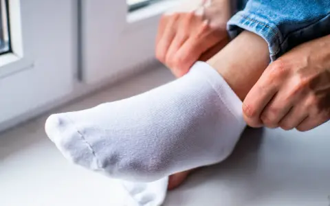 Dłonie naciągają białą skarpetkę na stopę. Dowiedz się, jak wybielić skarpetki, by znów były jak nowe.