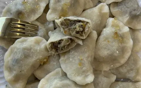 Pyszne pierogi z kapustą i pieczarkami, jeden przekrojony, by pokazać bogate nadzienie. Złoty widelec obok.