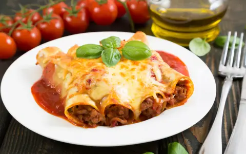 Cannelloni kontra naleśniki z mięsem: zapieczone w sosie pomidorowym i serze, ozdobione bazylią. Obok pomidorki i oliwa.