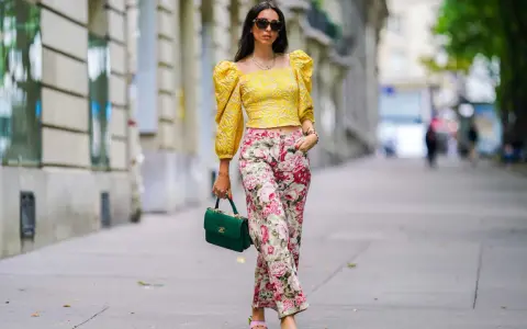 A woman shows that a woman can wear pants for cocktail attire, sporting a yellow puff-sleeve top and floral pants.