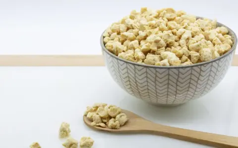 Un cuenco lleno de soja texturizada y una cuchara de madera con más de este ingrediente versátil.