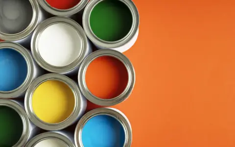 Un assortiment de pots de peinture glycero ou acrylique ouverts, révélant des couleurs vives comme le bleu, le jaune, le rouge, le vert et l'orange sur fond orange.