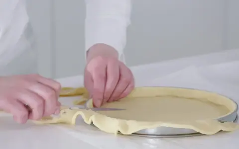 Préparation de la pâte pour une recette biscuit noisette. Les mains ajustent la pâte dans un moule à tarte.
