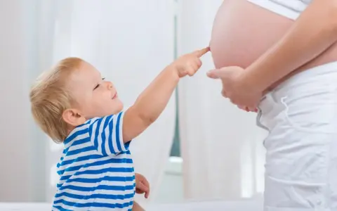 Mały chłopiec w pasiastej koszulce dotyka paluszkiem brzucha mamy, która jest w 25 tygodniu ciąży.