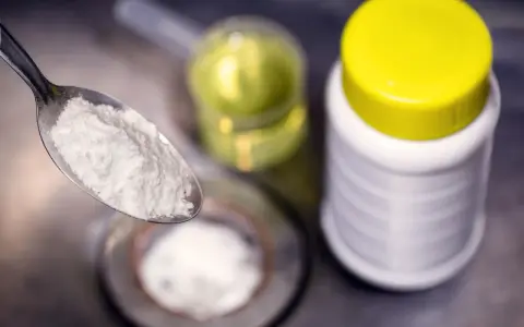 Ein Löffel mit weißem Pulver, bereit für die Reaktion mit Essig. Daneben ein Behälter mit Natron und eine Flasche mit Flüssigkeit.