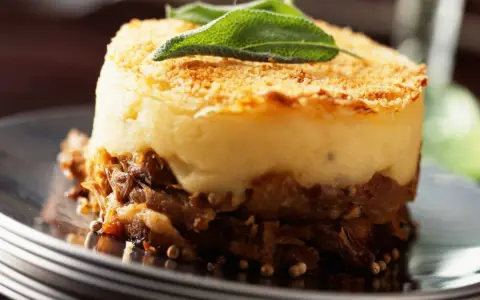 Un délicieux parmentier de canard, gratiné et garni d'une feuille de sauge, servi sur une assiette élégante.