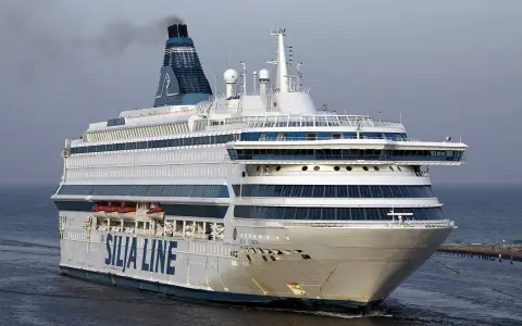 Ogromny prom pasażerski Silja Europa z charakterystycznym kominem i niebieskimi pasami na białym kadłubie płynie po spokojnym morzu.