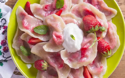 Pyszne pierogi z truskawkami, udekorowane miętą i śmietaną, na zielonym talerzu.