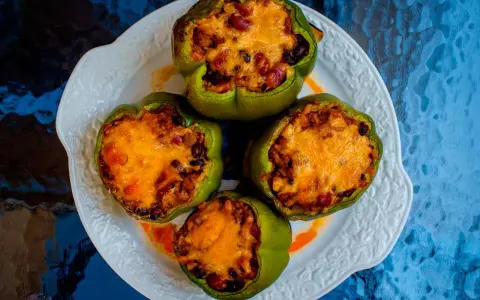 Cuatro pimientos verdes rellenos con carne, frijoles y arroz, cubiertos con queso derretido, servidos en un plato blanco.