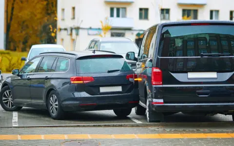 Ciemny kombi zaparkowany zbyt blisko drugiego samochodu, ledwo mieszcząc się na miejscu parkingowym.